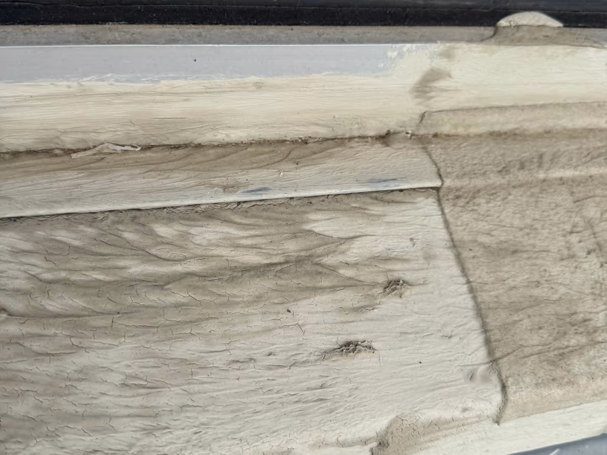 Traverse basse d'un châssis vitré en bois : peinture craquelée et farineuse, fibres du bois arrachées par endroits, joint de vitrage décollé