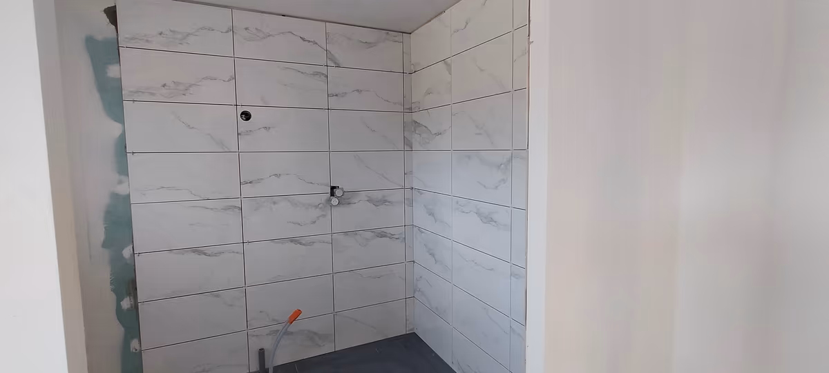 Douche en cours de finition, faïence grand format posée sur trois parois, attentes de robinetterie sorties et plaque hydrofuge encore visible en bordure