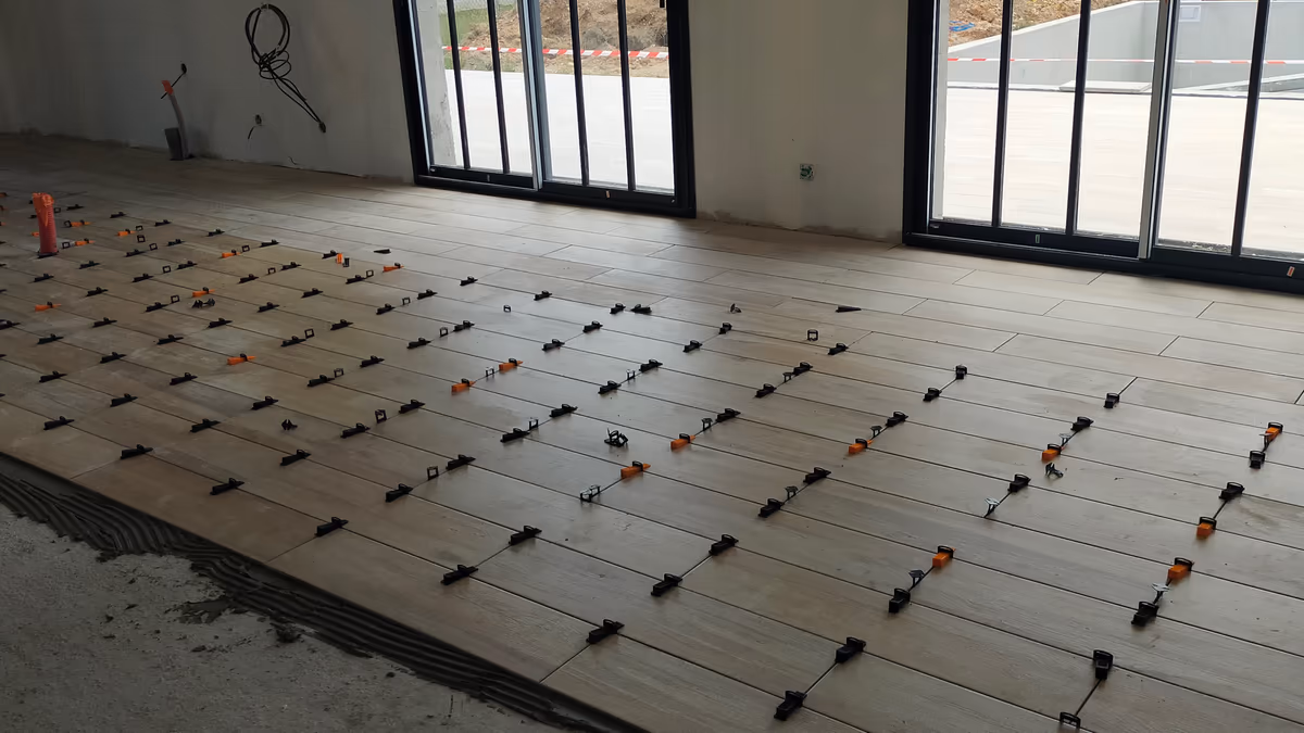 Carrelage de sol imitation bois en cours de pose dans une pièce neuve, système de calage autonivelant entre les lames et mortier-colle peigné encore à nu en bordure