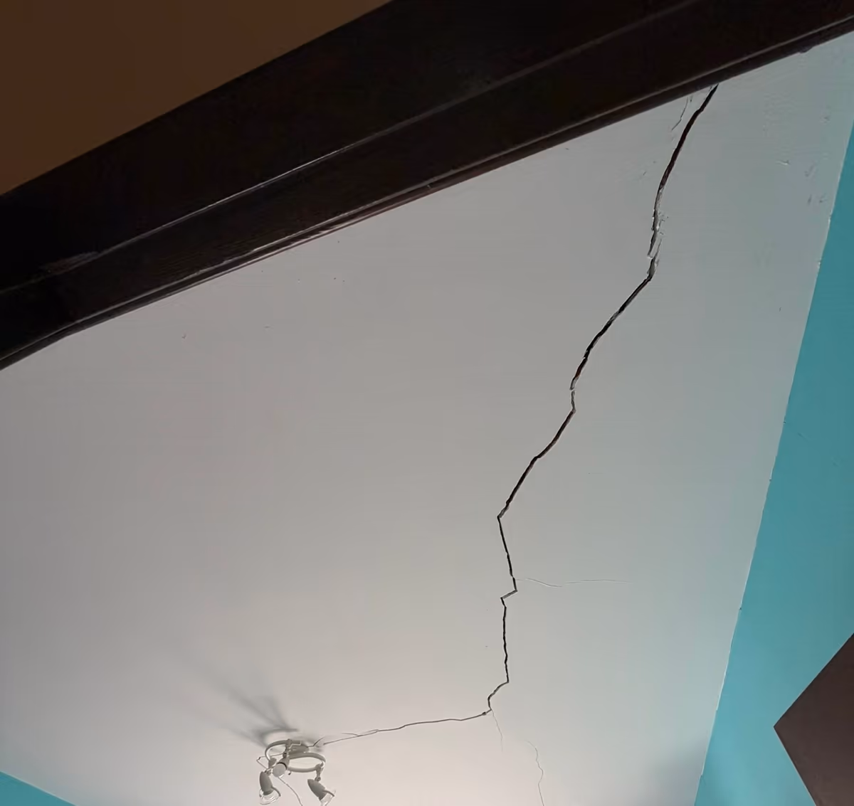 Fissure ouverte traversant le plafond d'une chambre en ligne brisée, depuis la rive d'une poutre jusqu'au point lumineux central