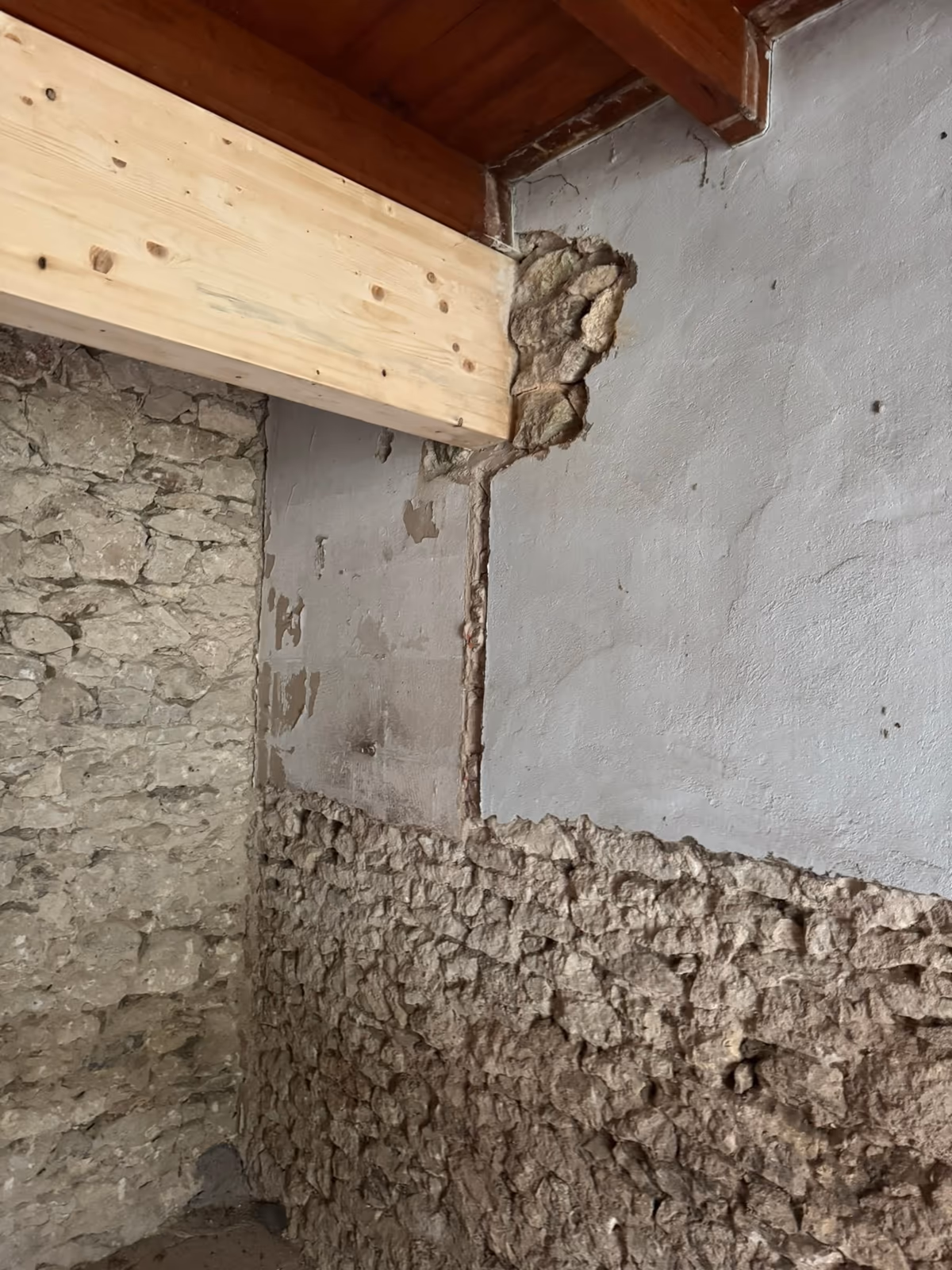 Poutre en bois neuf encastrée dans un mur ancien en moellons, scellement au mortier laissé brut et enduit interrompu au-dessus de la pierre nue