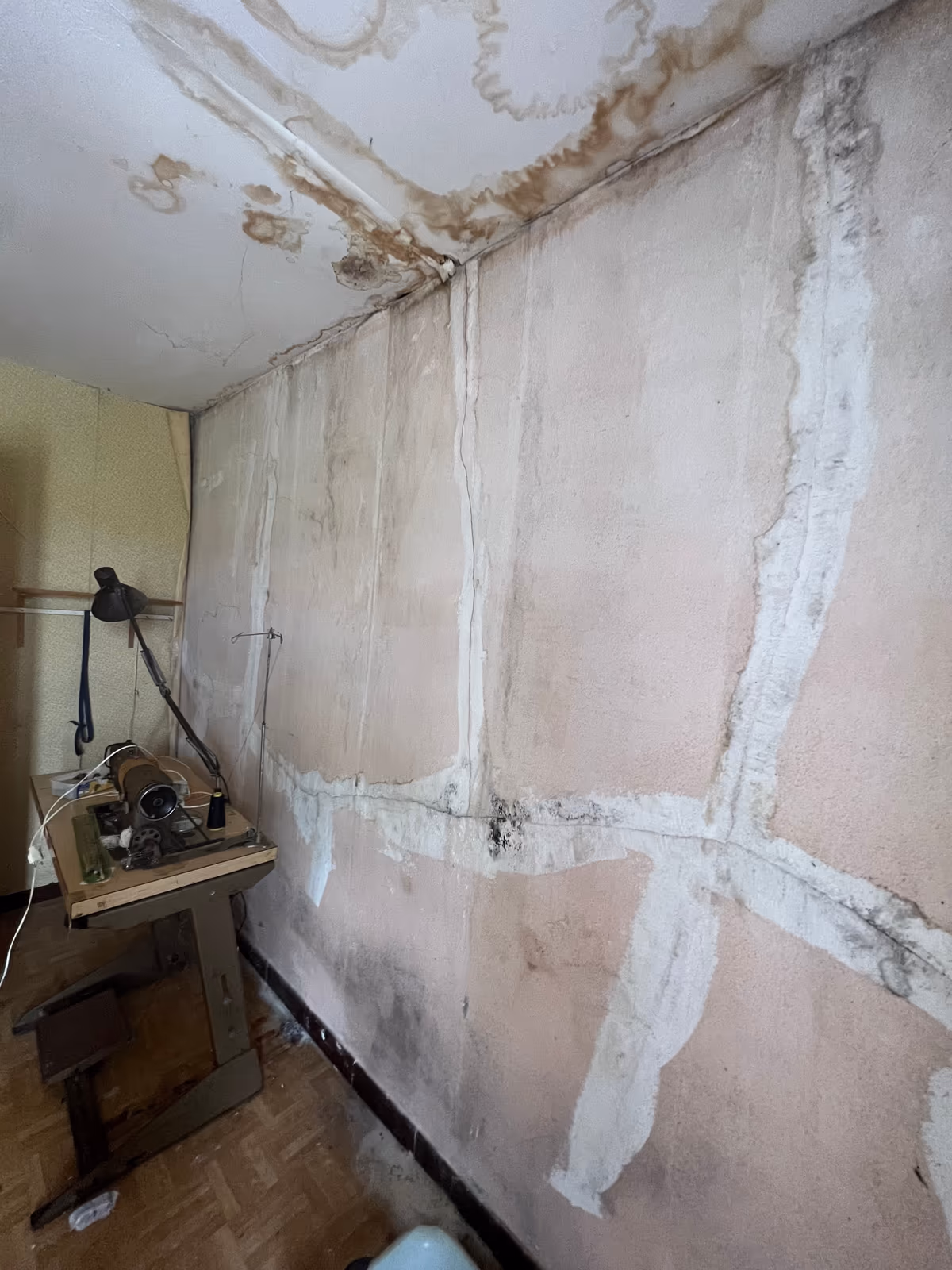 Mur intérieur aux fissures rebouchées à l’enduit blanc en larges bandes croisées, auréoles d’humidité au plafond et en tête de mur