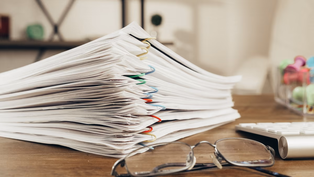 Dossier de diagnostics immobiliers posé sur une table : liasse épaisse de rapports agrafés par jeux de couleurs, lunettes posées à côté
