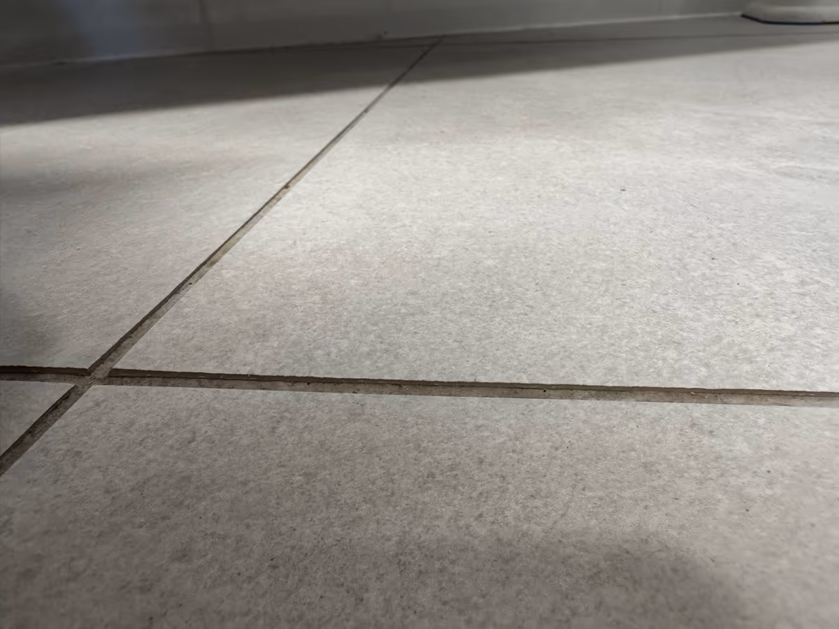 Carrelage de sol gris photographié au ras du sol, la lumière rasante soulignant la différence de niveau entre carreaux voisins le long des joints