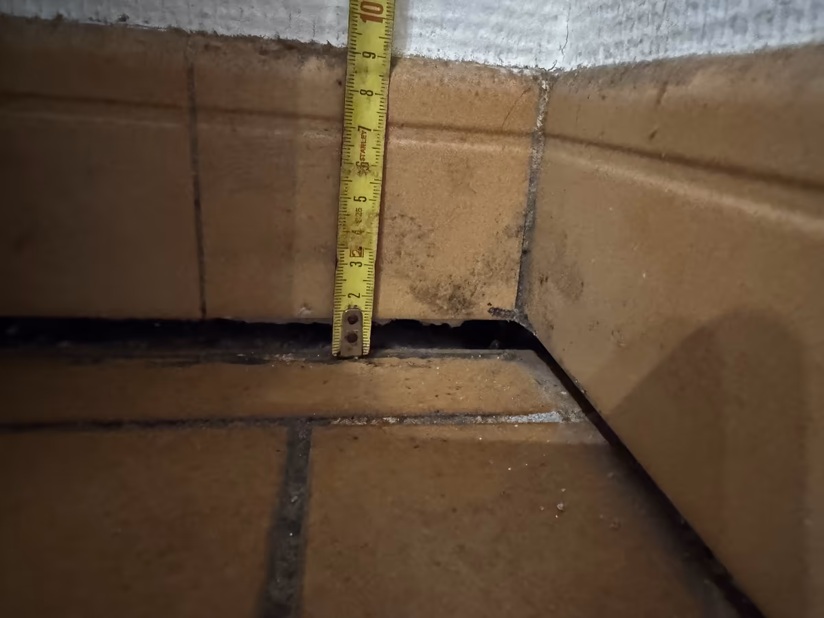 Mètre ruban posé dans un angle de pièce pour mesurer le vide ouvert entre une plinthe carrelée et le carrelage de sol