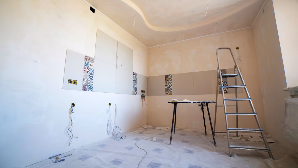 Pièce d'habitation en cours de travaux, faïence murale posée à mi-hauteur, murs enduits par plaques, escabeau et bâche de protection au sol
