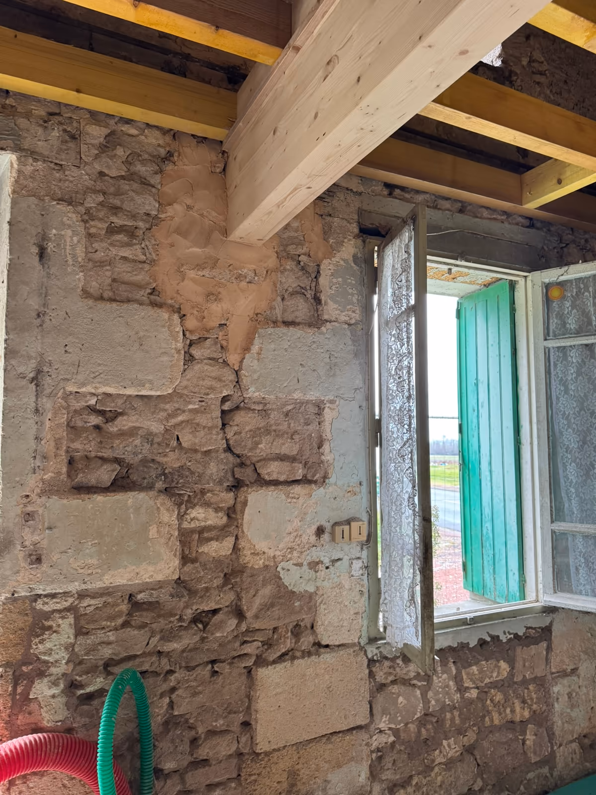 Mur intérieur en pierre de taille et moellons mis à nu sous un solivage bois neuf, avec des reprises au mortier d'époques différentes autour d'une fenêtre