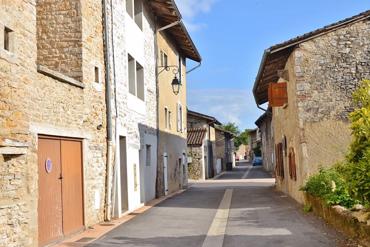 Rue étroite d'un bourg ancien français bordée de maisons en pierre implantées en limite de voie, portes de garage et façades ouvrant directement sur la chaussée