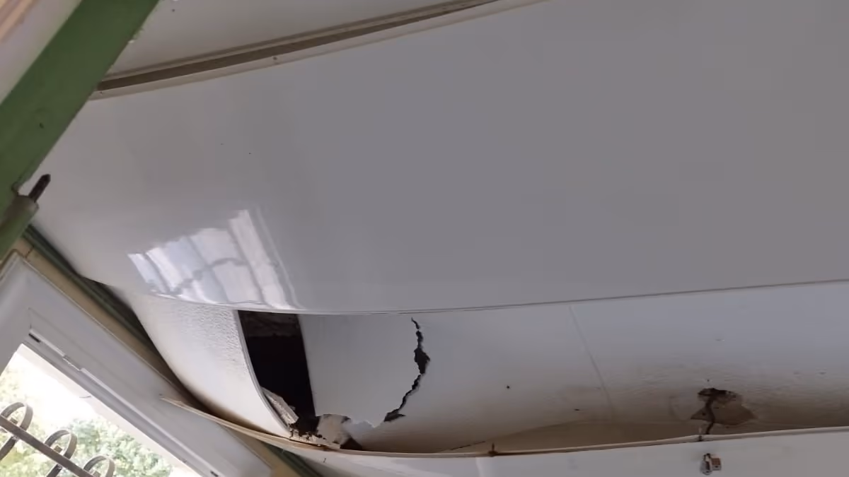 Plafond en lambris PVC affaissé et éventré près d'une fenêtre, lames déboîtées laissant voir le vide au-dessus après un sinistre