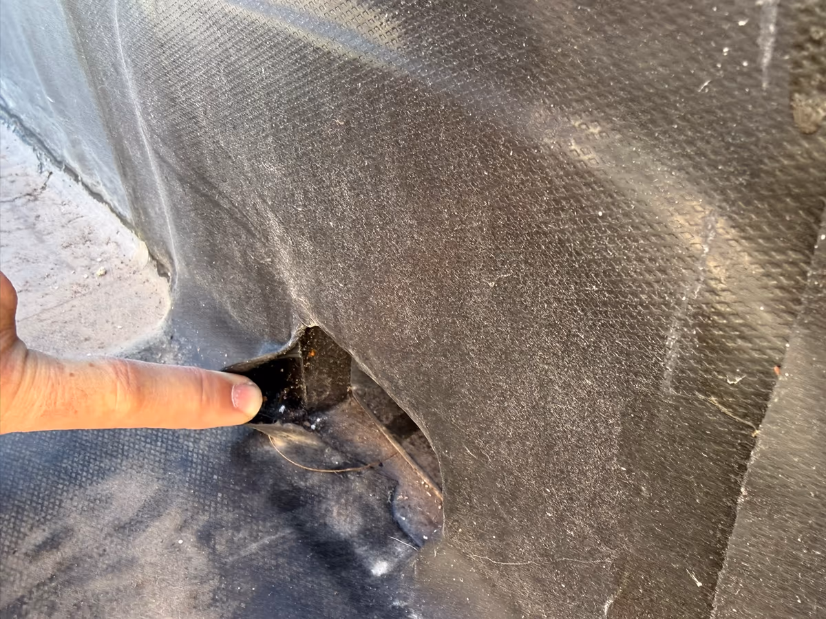 Doigt désignant un trou dans une membrane d'étanchéité, à l'angle où le relevé remonte contre la paroi d'une toiture-terrasse