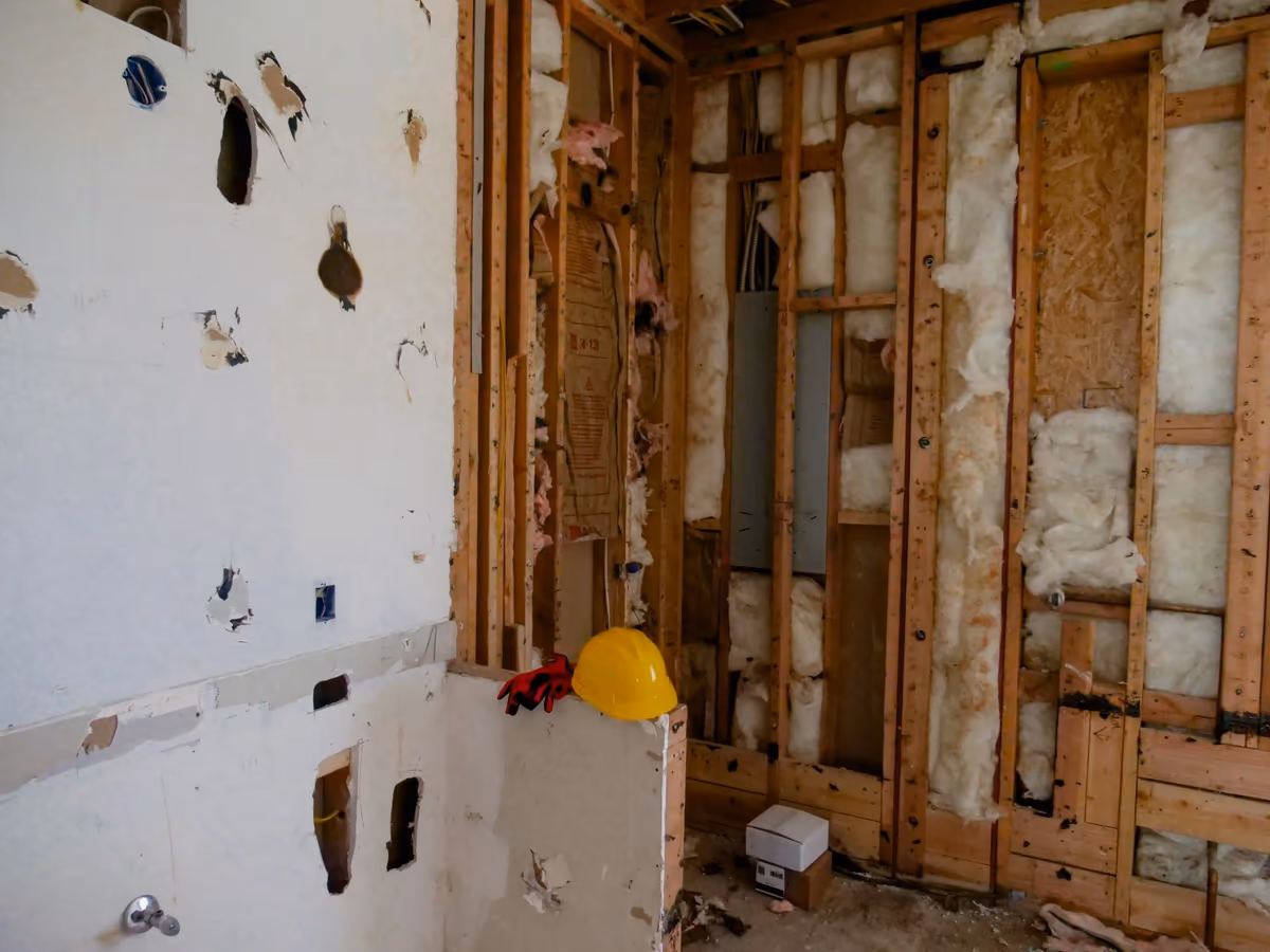 Cloison de doublage démontée dans une pièce en rénovation, ossature bois, laine minérale et boîtier électrique mis à nu derrière les plaques retirées
