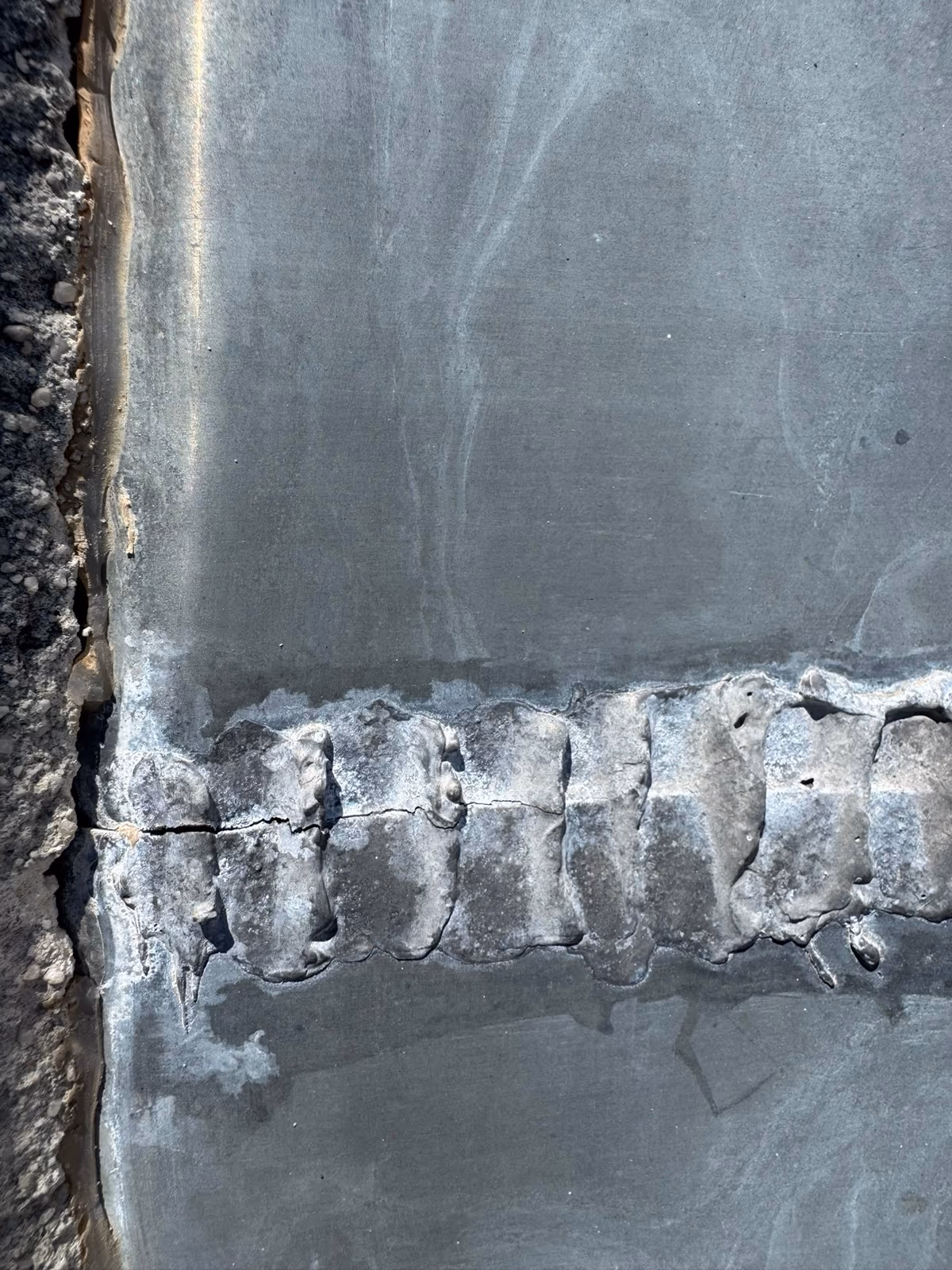 Bande de zinc reprise par une soudure épaisse et irrégulière, fissurée sur une partie de sa longueur, contre un mur enduit