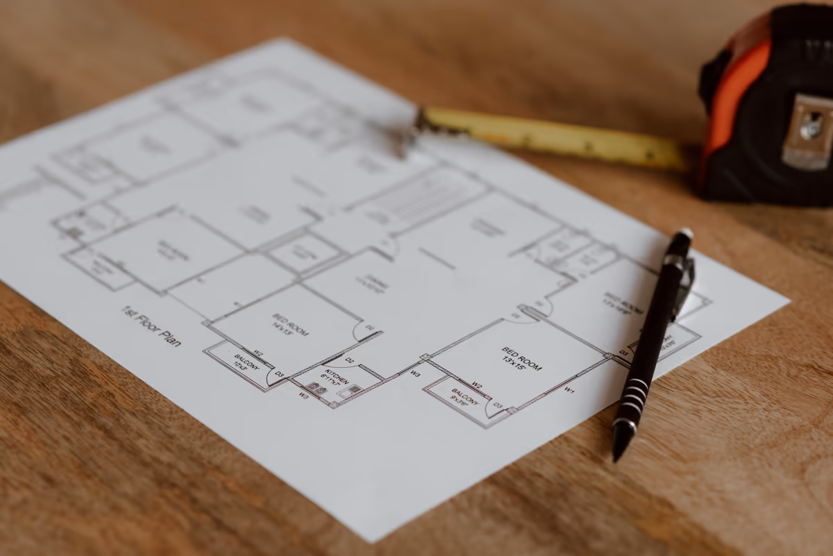 Plan de niveau d'un logement posé sur une table en bois, stylo et mètre ruban à côté, support de lecture d'un rapport d'expertise