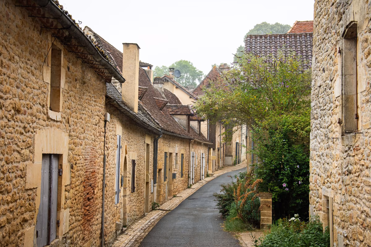 Rue étroite d'un bourg ancien bordée de maisons mitoyennes en pierre calcaire, façades jointives sans retrait et toitures accolées