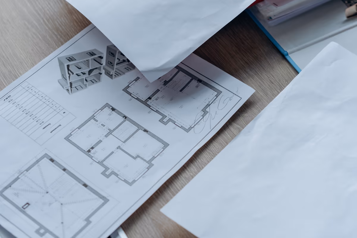 Plan de niveau d'une maison, feuilles et chemises d'un dossier de vente étalés sur une table de travail avant une visite d'expertise