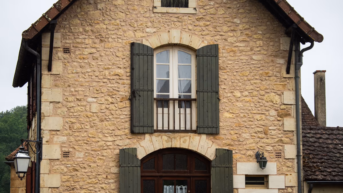 Façade d'une maison de bourg ancienne en pierre calcaire, encadrements taillés, volets bois et porte sous arc, vue depuis la rue