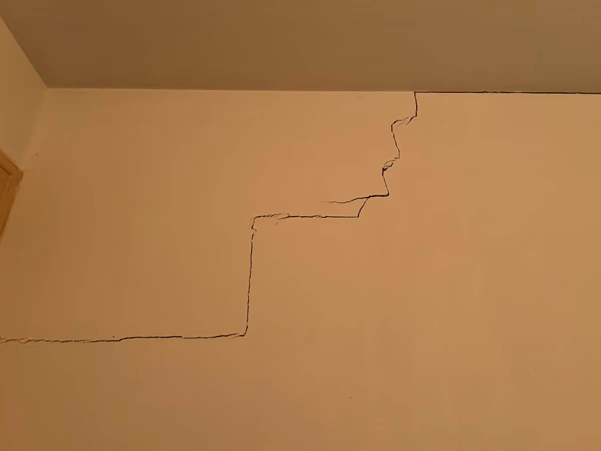 Fissure en escalier sur un mur intérieur enduit, partant de la jonction avec le plafond et descendant en marches régulières