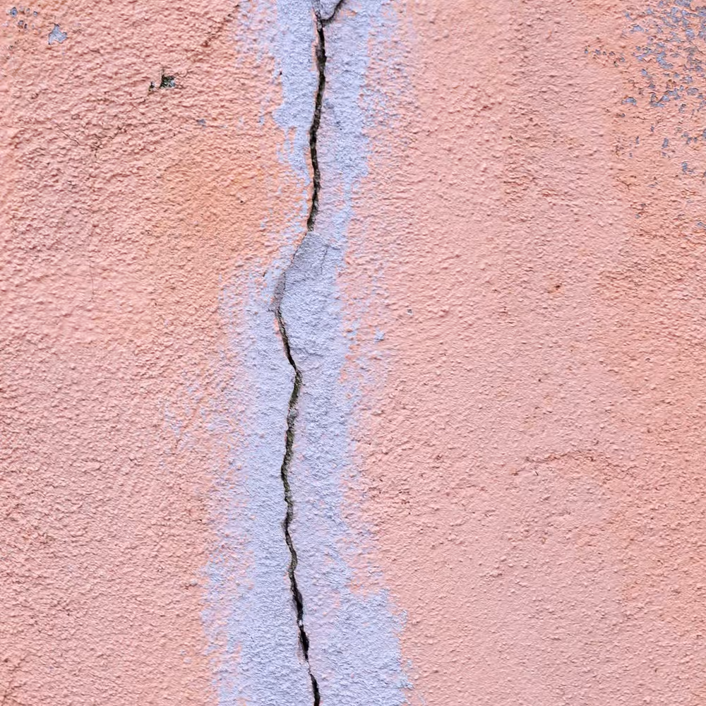 Fissure fine et rectiligne sur un mur de façade enduit, à peine marquée malgré son tracé continu sur toute la hauteur du cadre