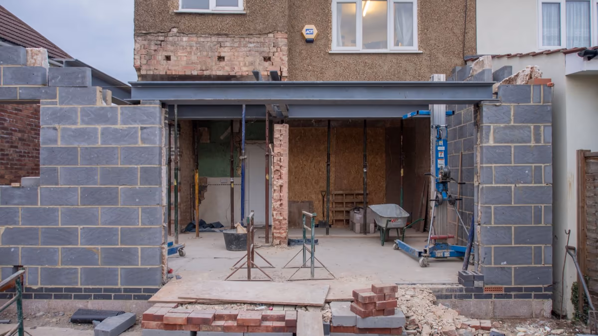 Extension de maison en cours de construction, poutre métallique posée sur les maçonneries et étais de reprise en place