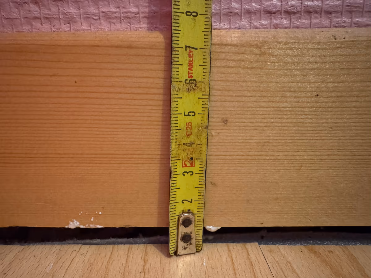Mètre pliant posé verticalement contre une plinthe en bois pour relever le jour ouvert entre la plinthe et le sol stratifié