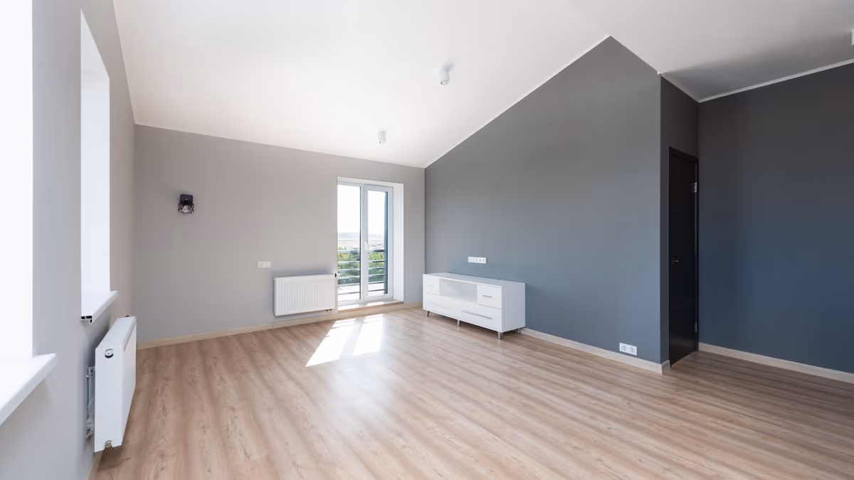 Séjour vide et achevé d'un logement livré, sol stratifié posé, radiateur et menuiseries en place, avant emménagement