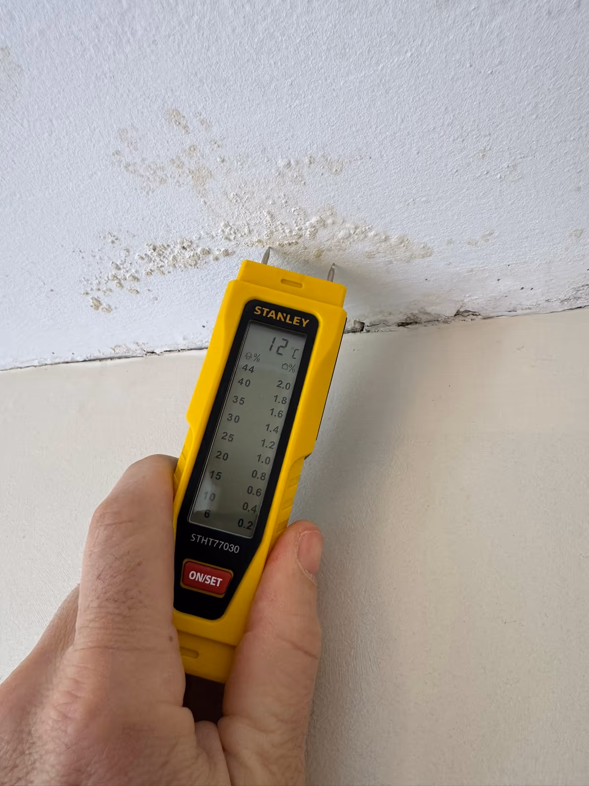 Humidimètre à pointes appliqué sur un enduit cloqué et taché, à la jonction d'un mur et d'un plafond