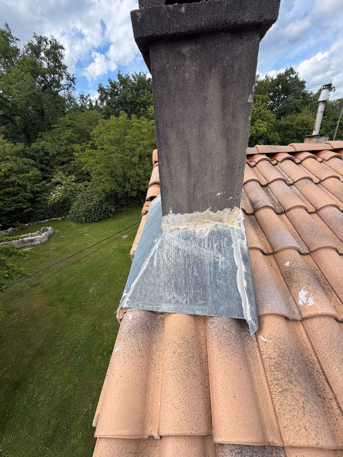Pied d'une souche de cheminée sur une couverture en tuiles, bavette en zinc rabattue sur les tuiles et joint de mastic craquelé contre la maçonnerie