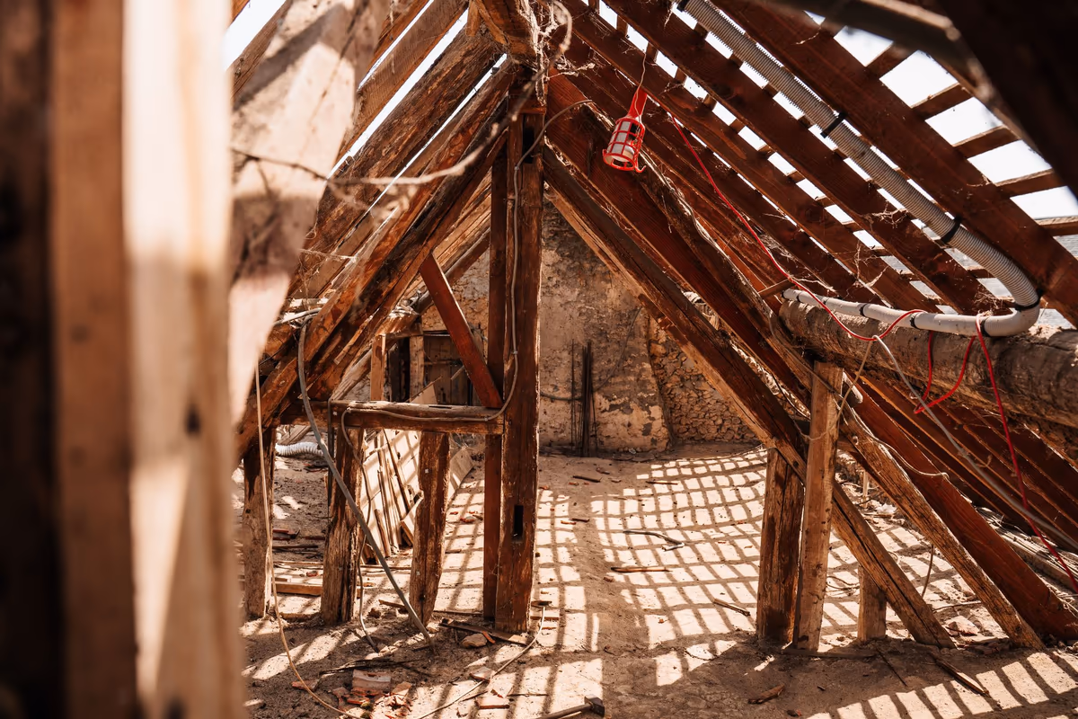 Comble d'une maison ancienne vu de l'intérieur : chevrons et liteaux d'une charpente traditionnelle, sous-face de la couverture sans écran de sous-toiture, jour visible entre les tuiles