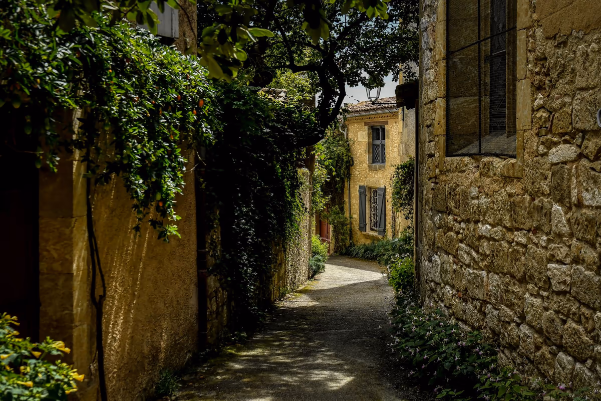 Ruelle étroite d'un centre ancien bordée de maisons mitoyennes en pierre calcaire, façades jointives ouvrant directement sur la voie