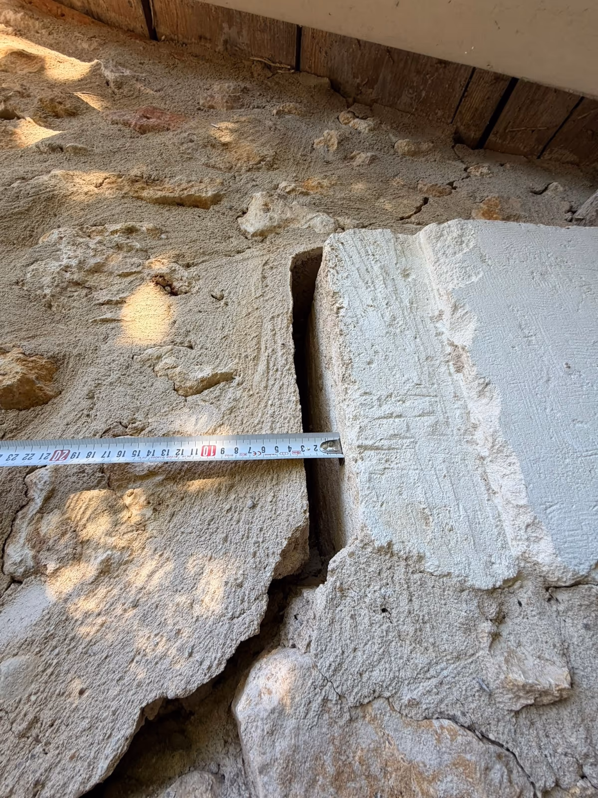 Mètre ruban tendu jusqu'au bord d'une pierre de taille séparée du mur de moellons voisin par une fissure ouverte, sous le débord de toit