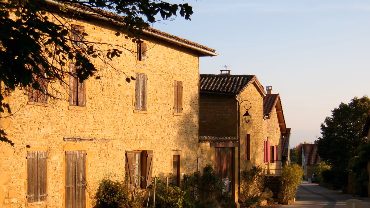 Alignement de maisons anciennes en pierre calcaire le long d'une rue de village, façades mitoyennes, volets bois et toitures en tuiles canal