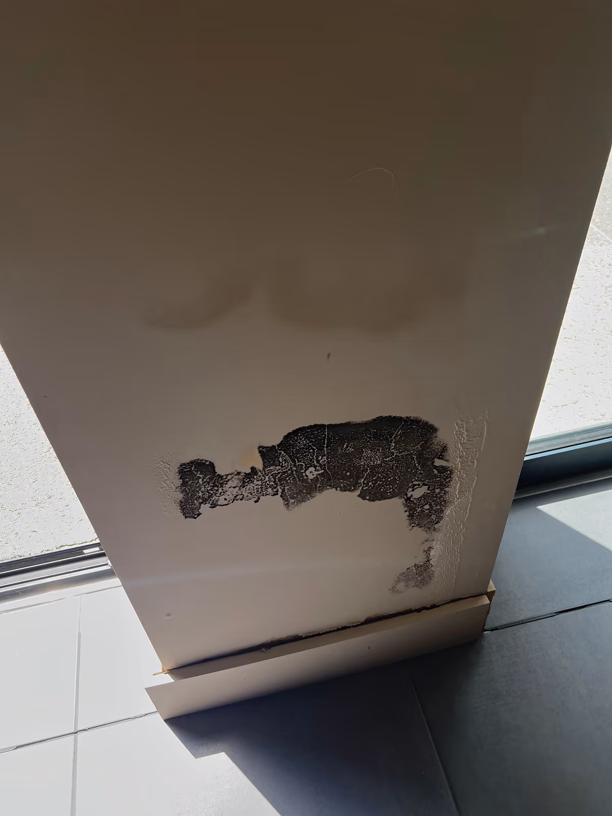 Bas d'un parement intérieur en plaque de plâtre peint, dont le papier de surface s'est arraché en une large plaque noircie juste au-dessus de la plinthe, avec une auréole plus haut