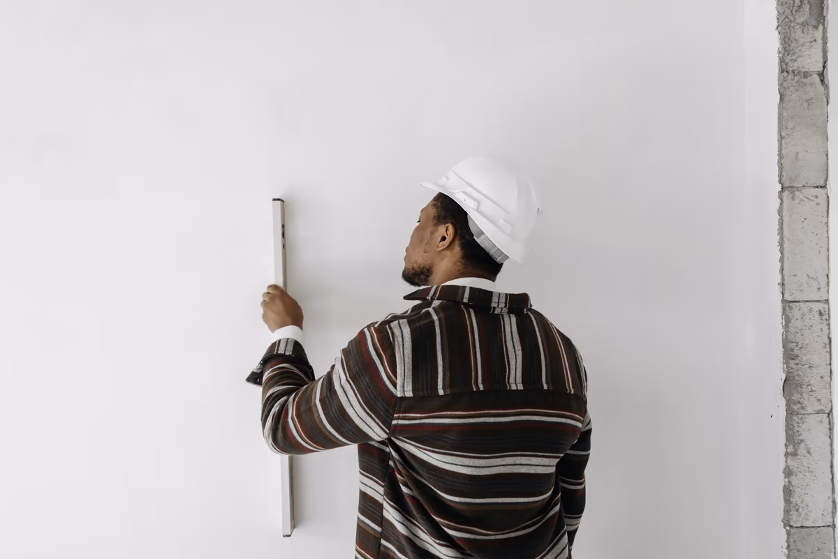 Homme casqué appliquant une règle de niveau contre un mur intérieur pour en contrôler la verticalité sur un chantier
