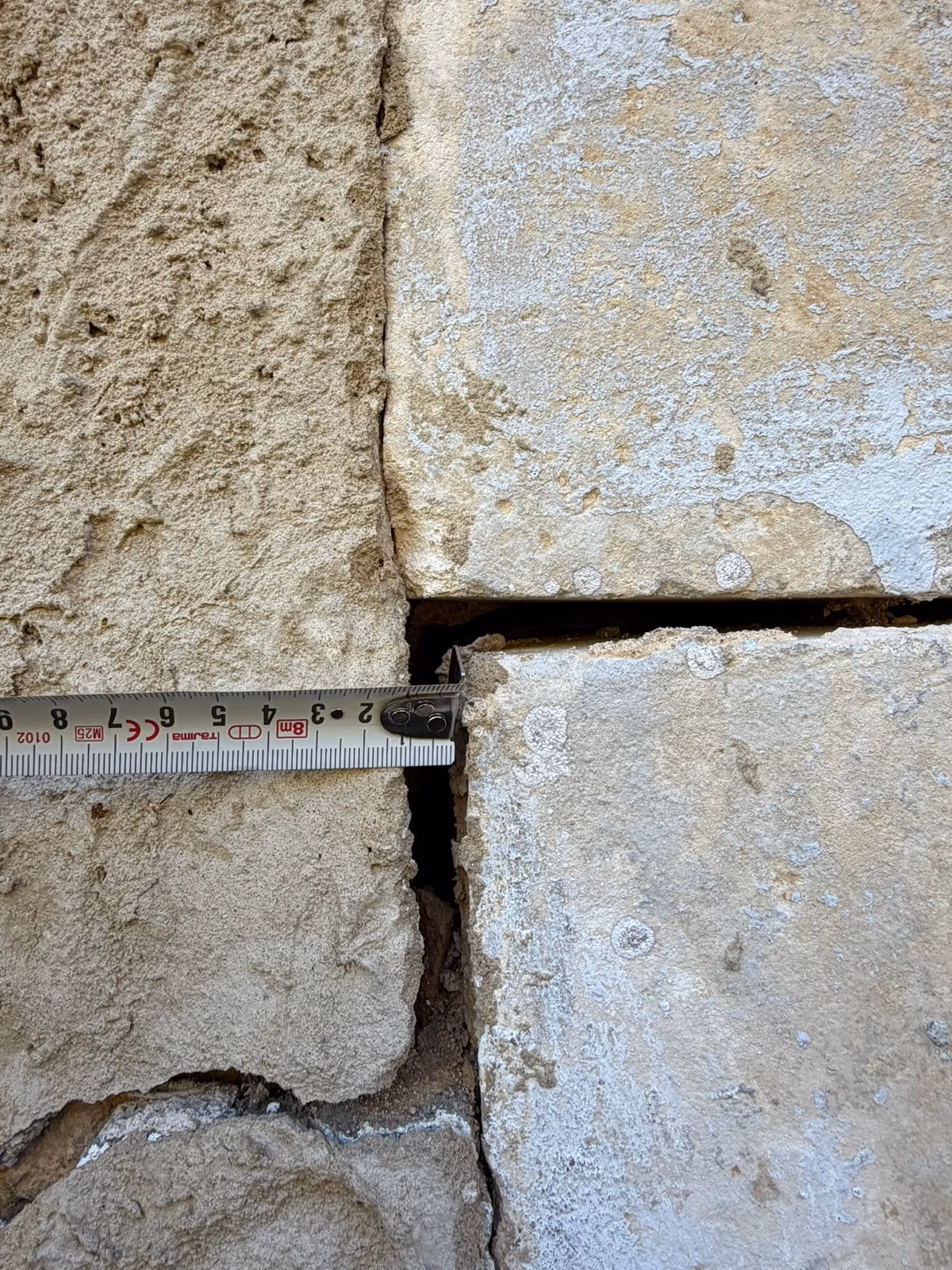 Mètre ruban appliqué contre un jambage en pierre de taille dont deux blocs se sont décalés, laissant un vide ouvert entre eux