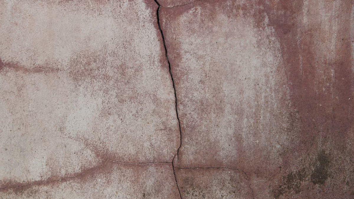 Mur enduit de maison individuelle portant une fissure traversante verticale et des traces d'humidité en surface