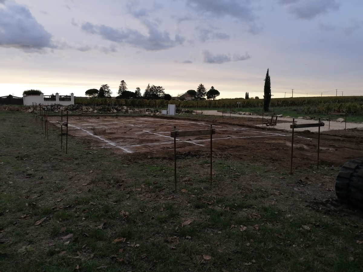Implantation d'une maison neuve sur un terrain nu : chaises en bois et tracés à la chaux délimitant l'emprise des fondations