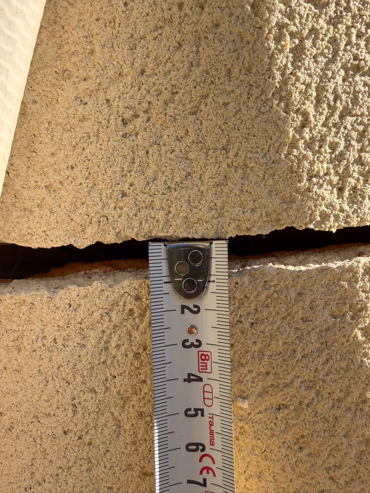 Mètre ruban posé en travers d'une fissure horizontale largement ouverte dans un enduit de façade pour en relever l'ouverture