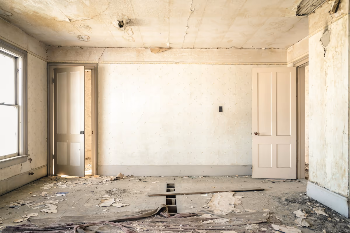 Pièce d'habitation dont le plancher bois est éventré sur toute une travée, plafond fissuré et lambeaux de revêtement au sol