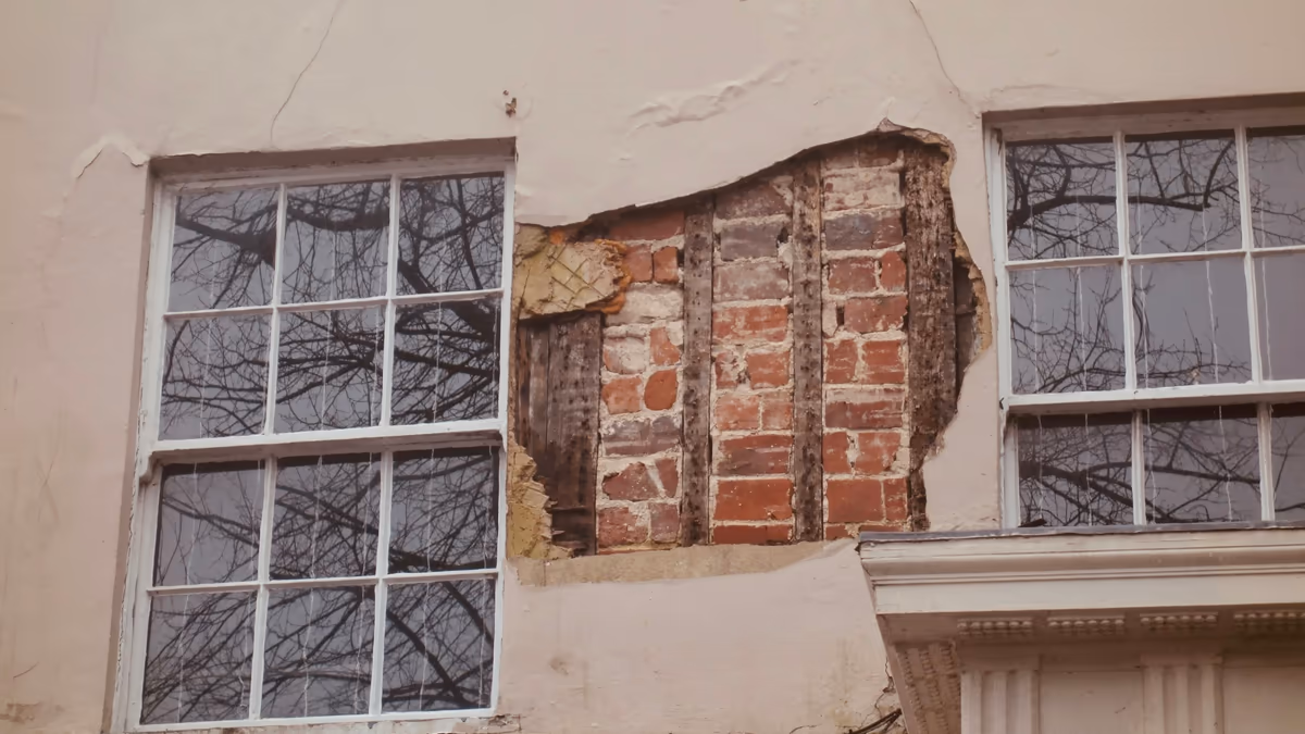 Façade de maison ancienne dont l'enduit s'est détaché entre deux fenêtres, laissant la maçonnerie de brique à nu